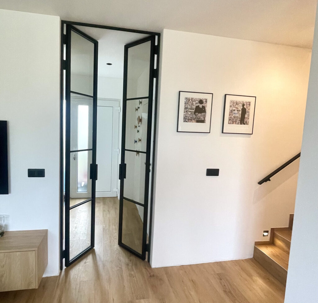 Ocelové dveře se sklem v interiéru mezi chodbou a obývací částí.